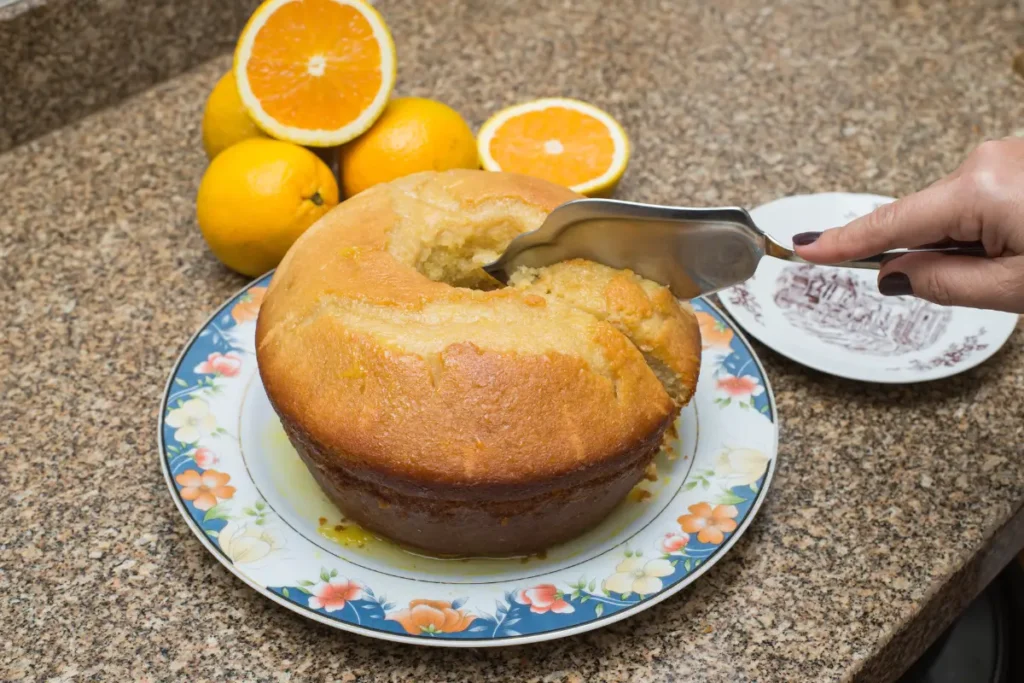 uma-mulher-partindo-um-bolo-de-laranja-e-tem-algumas-laranjas-na-mesa