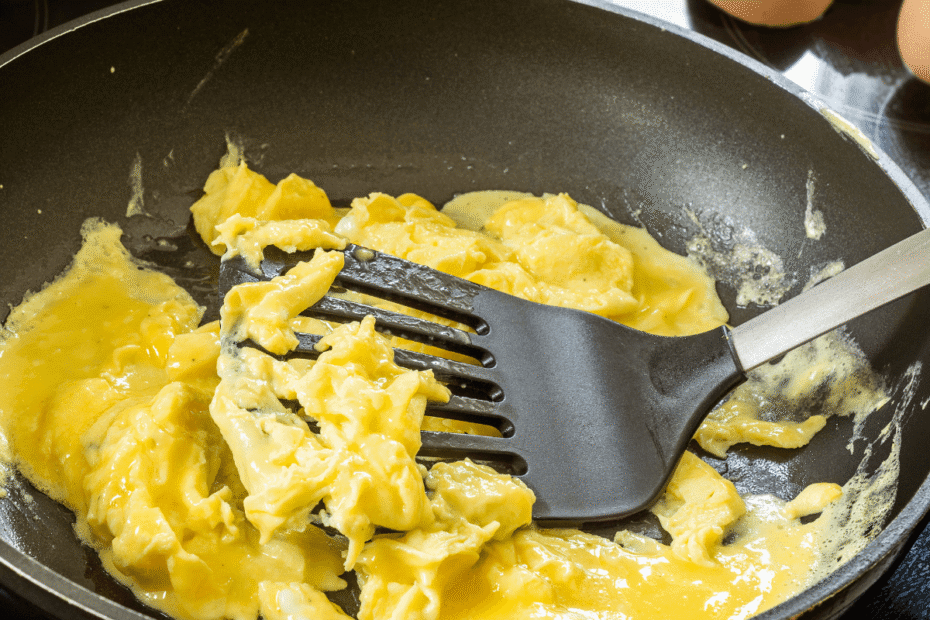 Ovos sendo preparados na frigideira com auxílio de uma espátula, ilustrando o desafio comum de evitar que o alimento grude no fundo durante a fritura matinal.