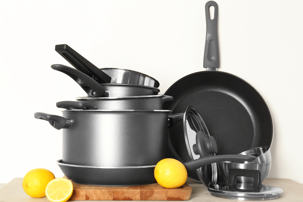 Pilha de panelas e frigideiras com revestimento sintético cinza, exemplificando utensílios vulneráveis à degradação da camada antiaderente por superaquecimento e abrasão.