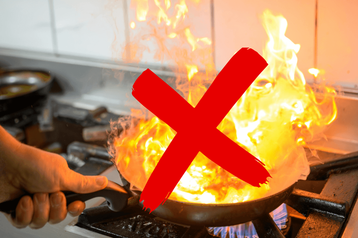 Frigideira antiaderente envolta em chamas altas com um X vermelho grande por cima, ilustrando o erro grave de superaquecimento que destrói o revestimento.