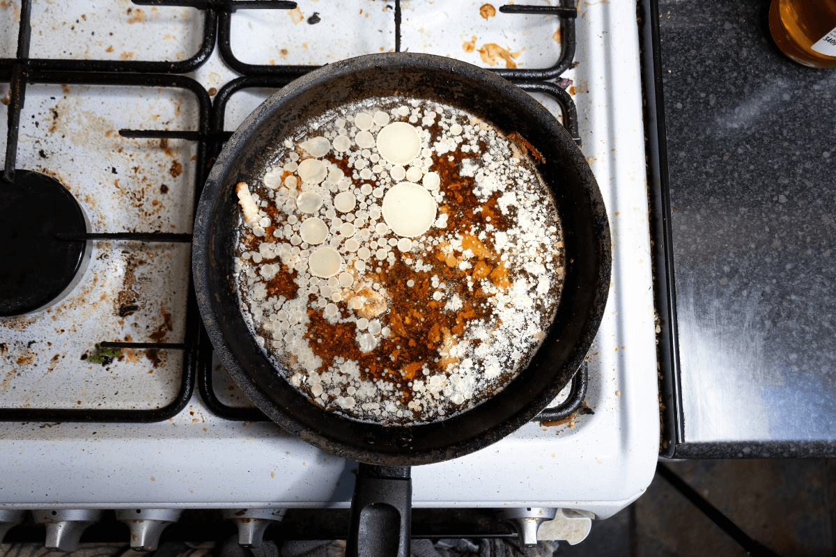 Interior de uma frigideira suja com gordura carbonizada e resíduos queimados, mostrando como a falta de limpeza correta estraga a frigideira antiaderente.