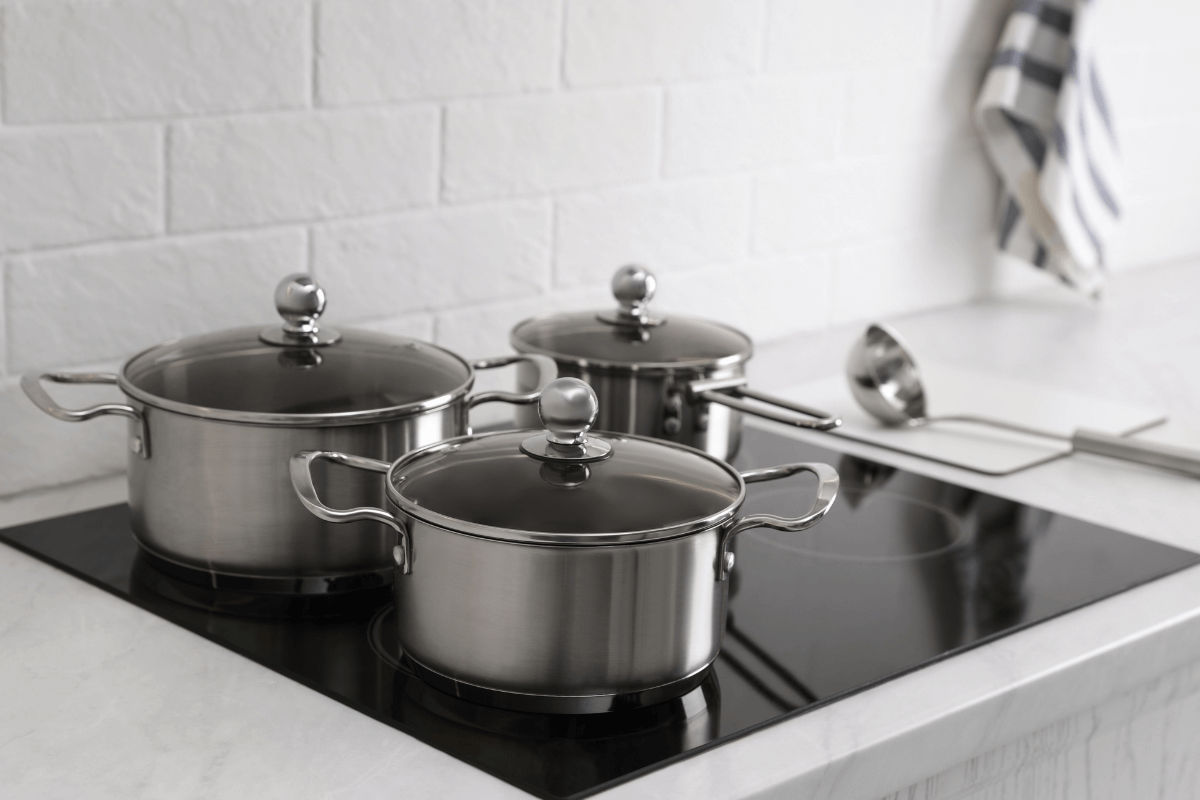 Panelas de aço inox com tampas de vidro sobre cooktop de indução preto, ilustrando o contato do fundo plano com a superfície vitrocerâmica.