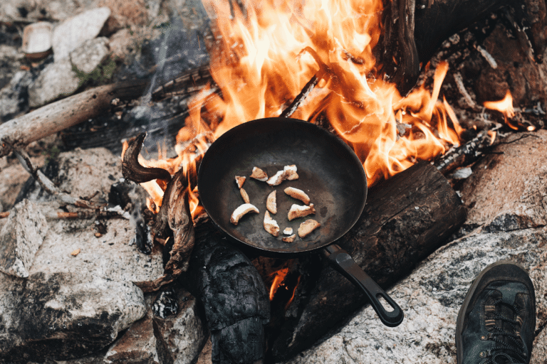 Frigideira robusta sendo utilizada diretamente sobre uma fogueira com chamas altas, ilustrando a durabilidade de materiais que não descascam mesmo sob condições extremas de calor.