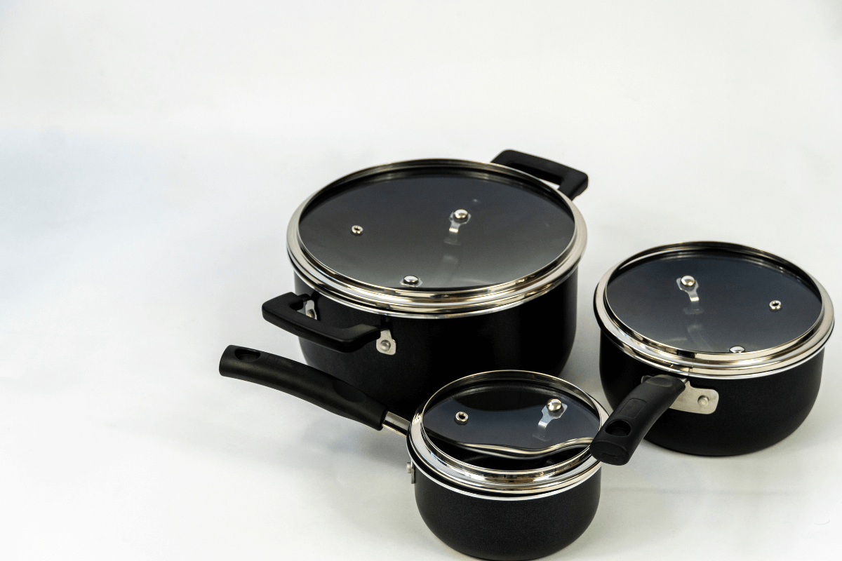 Jogo de panelas pretas antiaderentes com tampas de vidro temperado e orifício para saída de vapor, detalhando o aro de metal para vedação nas bordas.