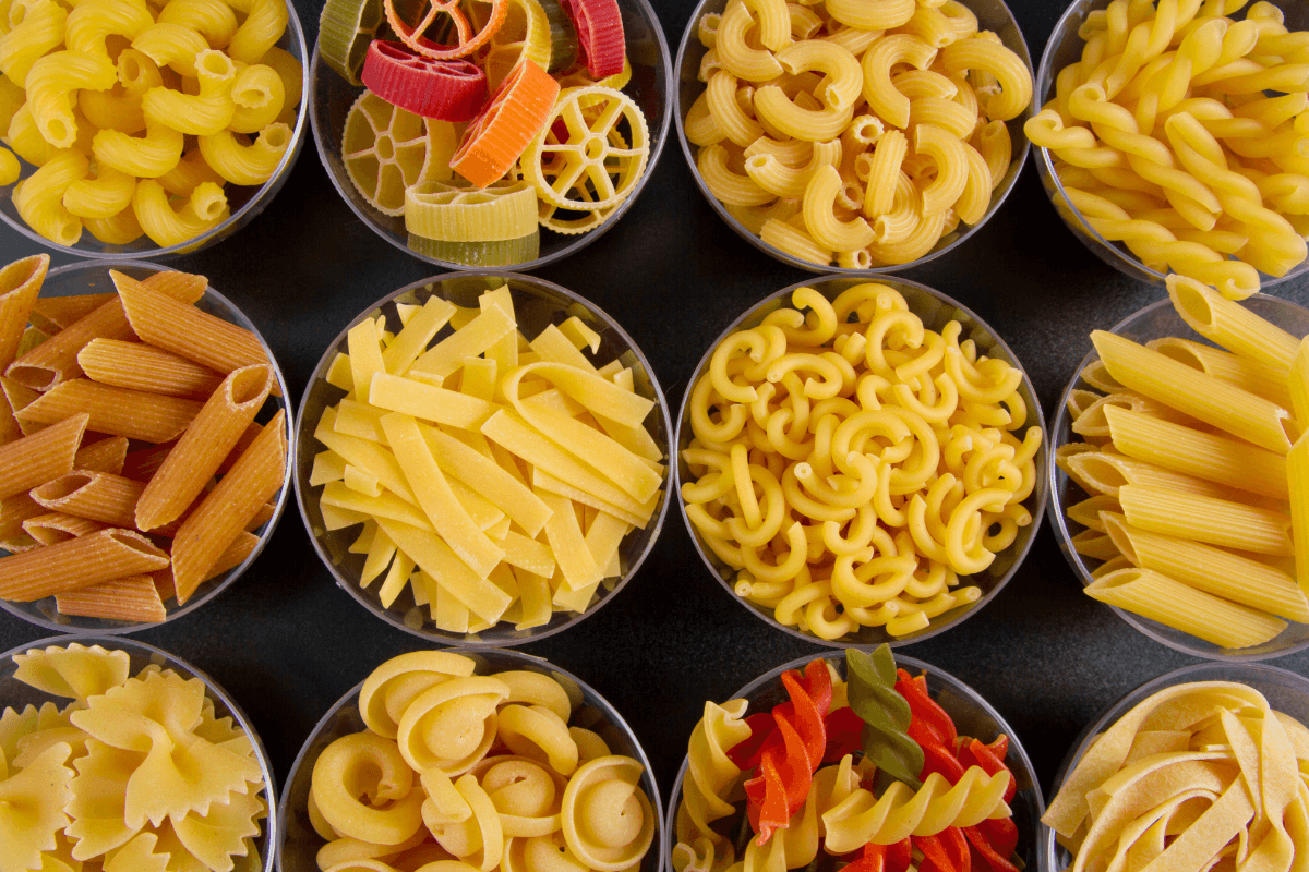 Variedade de massas cruas em tigelas, ilustrando os tipos de macarrão que podem ser preparados na panela elétrica de arroz.