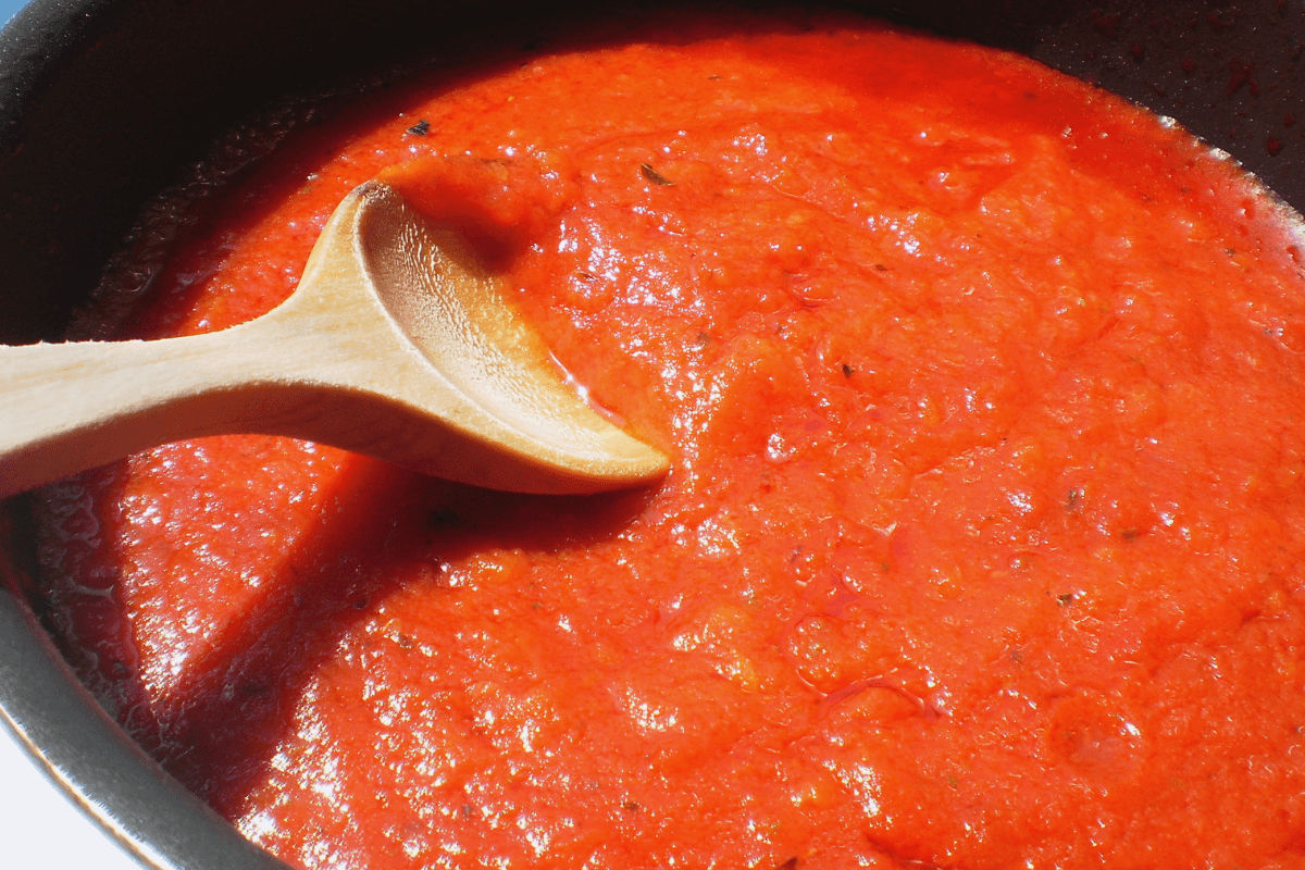 Colher de madeira mexendo um molho de tomate denso em uma panela antiaderente, ilustrando o risco que a acidez excessiva traz para a integridade do revestimento químico.