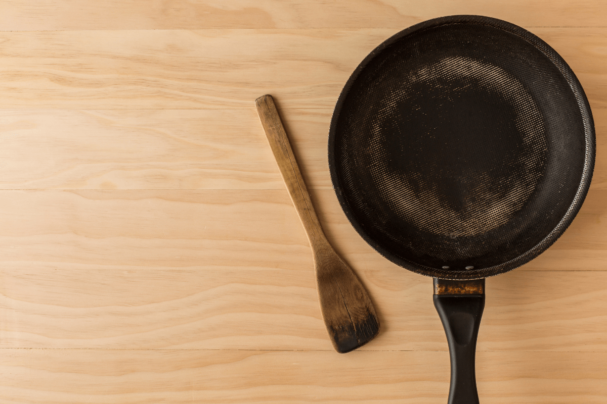 Frigideira antiaderente com o fundo visivelmente gasto e riscado sobre uma mesa de madeira, ilustrando o resultado final dos hábitos que destroem o revestimento.