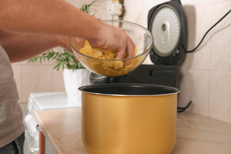 Homem despejando batatas picadas na cuba da panela elétrica, demonstrando na prática a versatilidade de preparo de outros alimentos além do arroz.