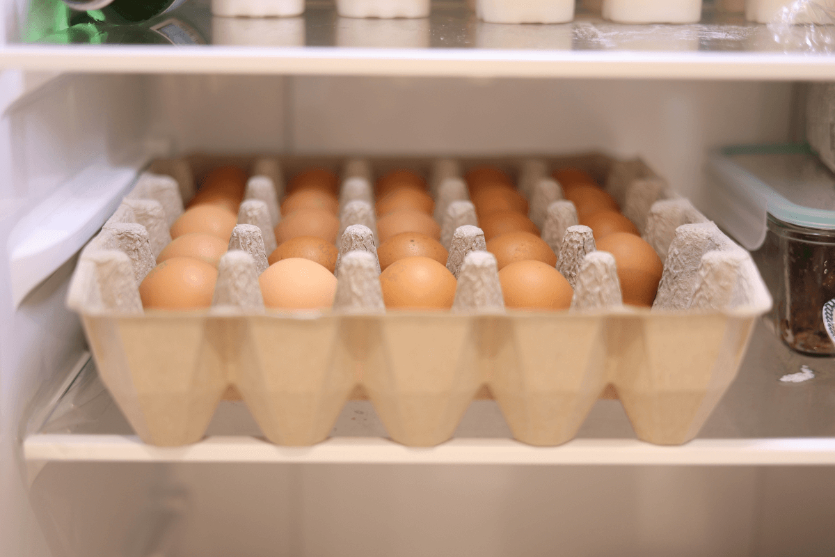 Cartela com ovos na prateleira da geladeira, ilustrando a discussão sobre o impacto da temperatura fria do ingrediente na aderência da frigideira.