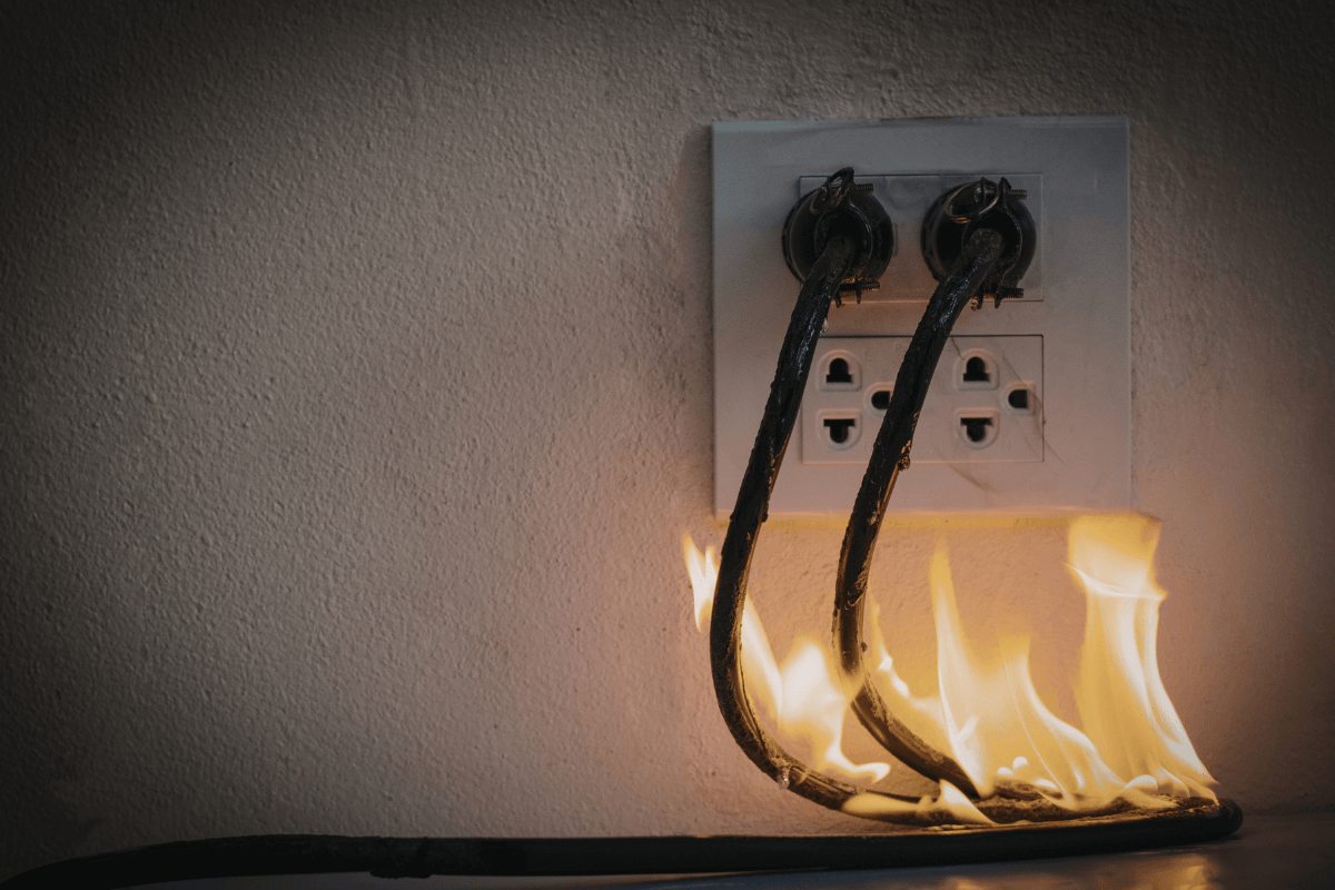 Perigo: O que acontece se ligar na voltagem errada? Fios e tomada pegando fogo ilustrando o perigo de ligar panela elétrica na voltagem errada ou sobrecarga na rede.