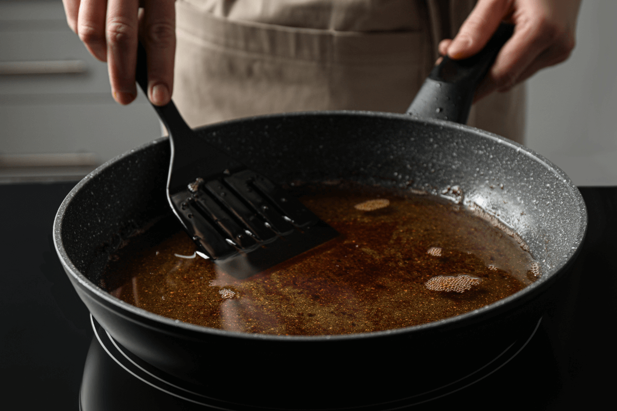 Fritura em frigideira escura com revestimento antiaderente e espátula preta, ilustrando o tipo de utensílio que exige cuidado para não liberar toxinas ou metais pesados na comida quando aquecido.