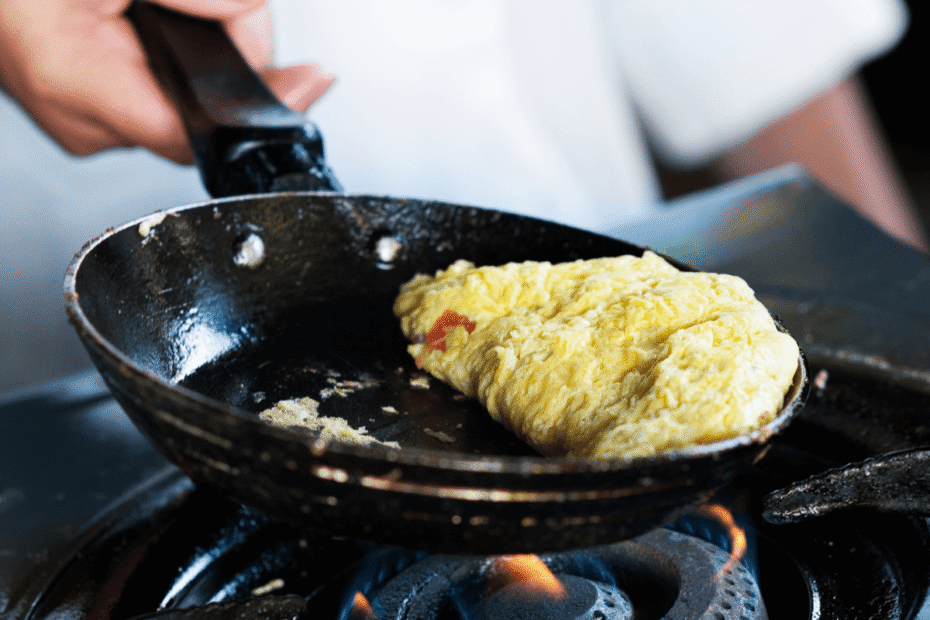 Omelete sendo preparado em uma frigideira sobre a chama do fogão, ilustrando o momento em que se percebe porque a frigideira antiaderente gruda devido a resíduos ou desgaste.