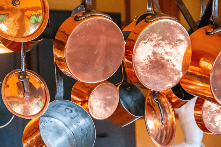 Várias panelas de metal penduradas em uma cozinha, ilustrando o guia sobre quais são os 6 tipos de panelas e qual é a mais segura para a saúde.