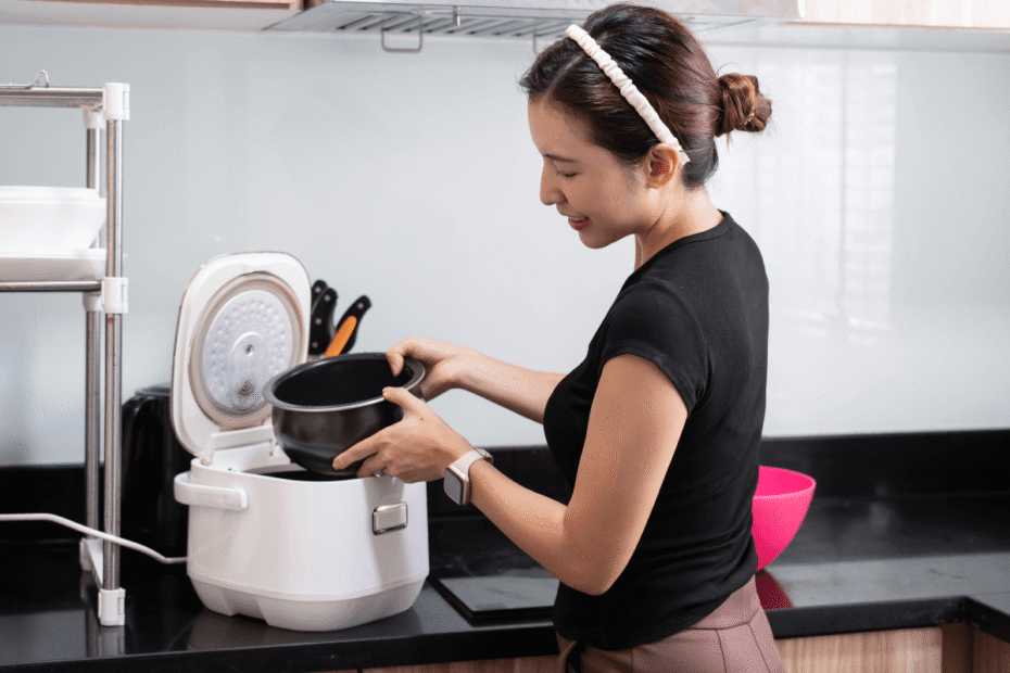 Mulher sorrindo ao encaixar a cuba na base, demonstrando na prática qual a vantagem de ter uma panela de arroz elétrica pela simplicidade de uso.