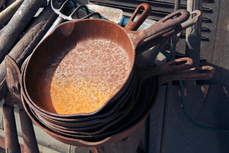 Pilha de frigideiras de ferro fundido antigas e tomadas pela ferrugem, ilustrando visualmente o estado de degradação e os tipos de utensílios que devem ser evitados na cozinha para prevenir intoxicação.