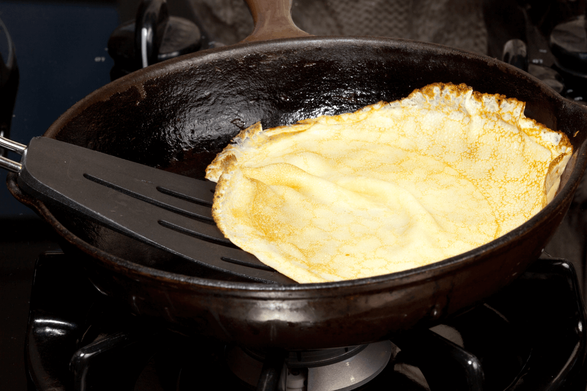 Espátula de nylon virando uma massa em frigideira com revestimento íntegro e sem riscos, demonstrando a importância de manter a superfície lisa para a segurança alimentar.