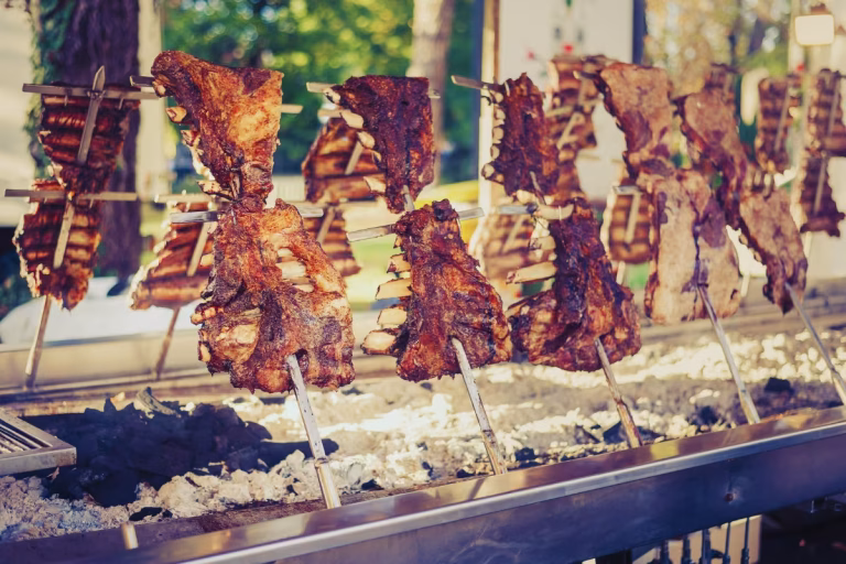 Costelas de boi assando no formato de parrilla argentina, suspensas com uma leve inclinação dos espetos de aço.