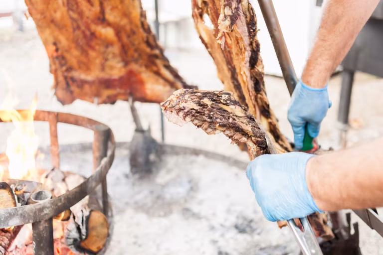 Homem espetando a carne bovina e colocando sob a brasa no estilo parrilla uruguaia.